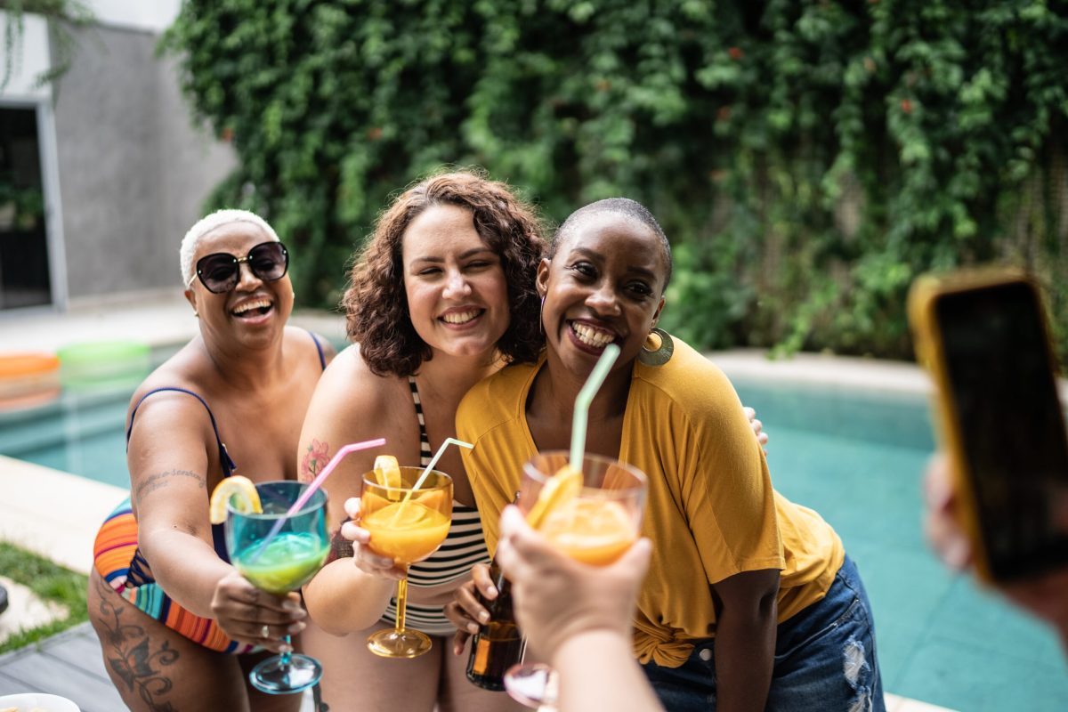 Friends taking a photo holding drinks during pool party at home